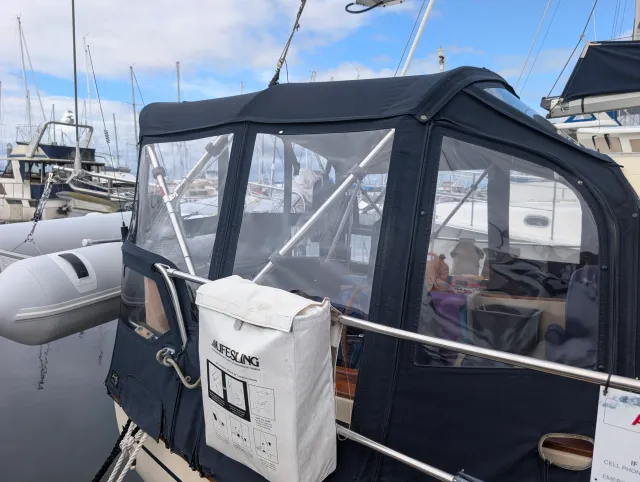The aft side of a navy canvas and clear vinyl enclosure on a sailboat at the dock, with a white Lifesling bag on the rail.