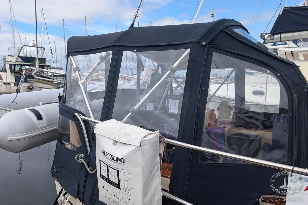The aft side of a navy canvas and clear vinyl enclosure on a sailboat at the dock, with a white Lifesling bag on the rail.