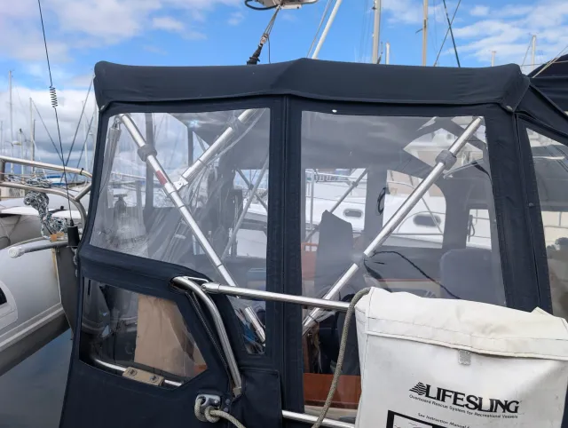 Close view of two clear vinyl windows in the aft enclosure curtain, with stainless steel frame tubes running diagonally behind the vinyl.