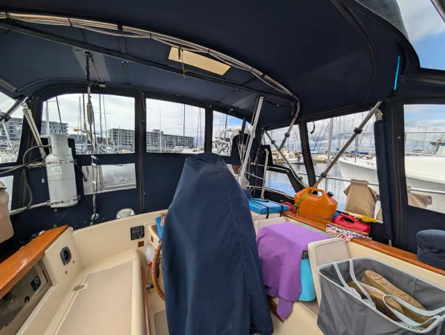 Inside the enclosed cockpit looking aft, with navy canvas walls, clear vinyl windows and the covered wheel in the foreground.
