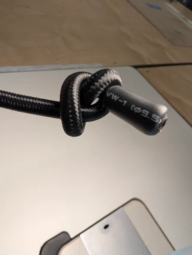 Close view of a black shock cord tied in a knot, its cut end finished in a black heat-shrink sleeve.